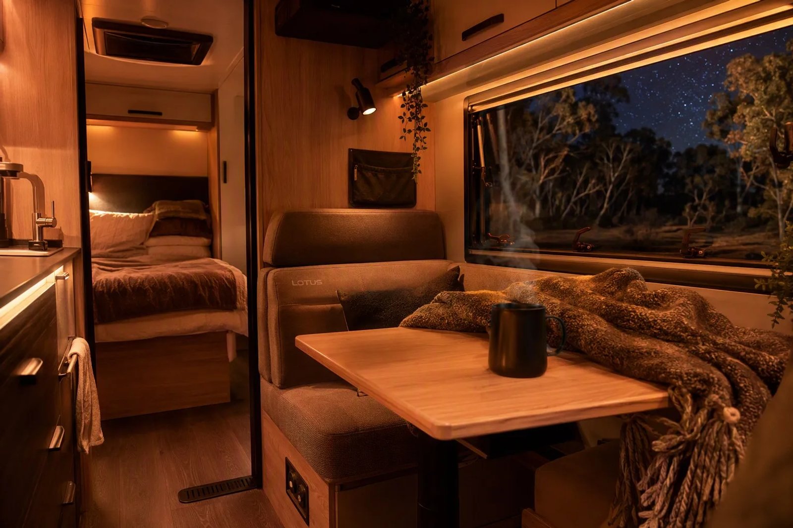 Warm interior of an Australian caravan at night showing a diesel heater vent bathed in amber LED light with a cold starry outback sky visible through the window.