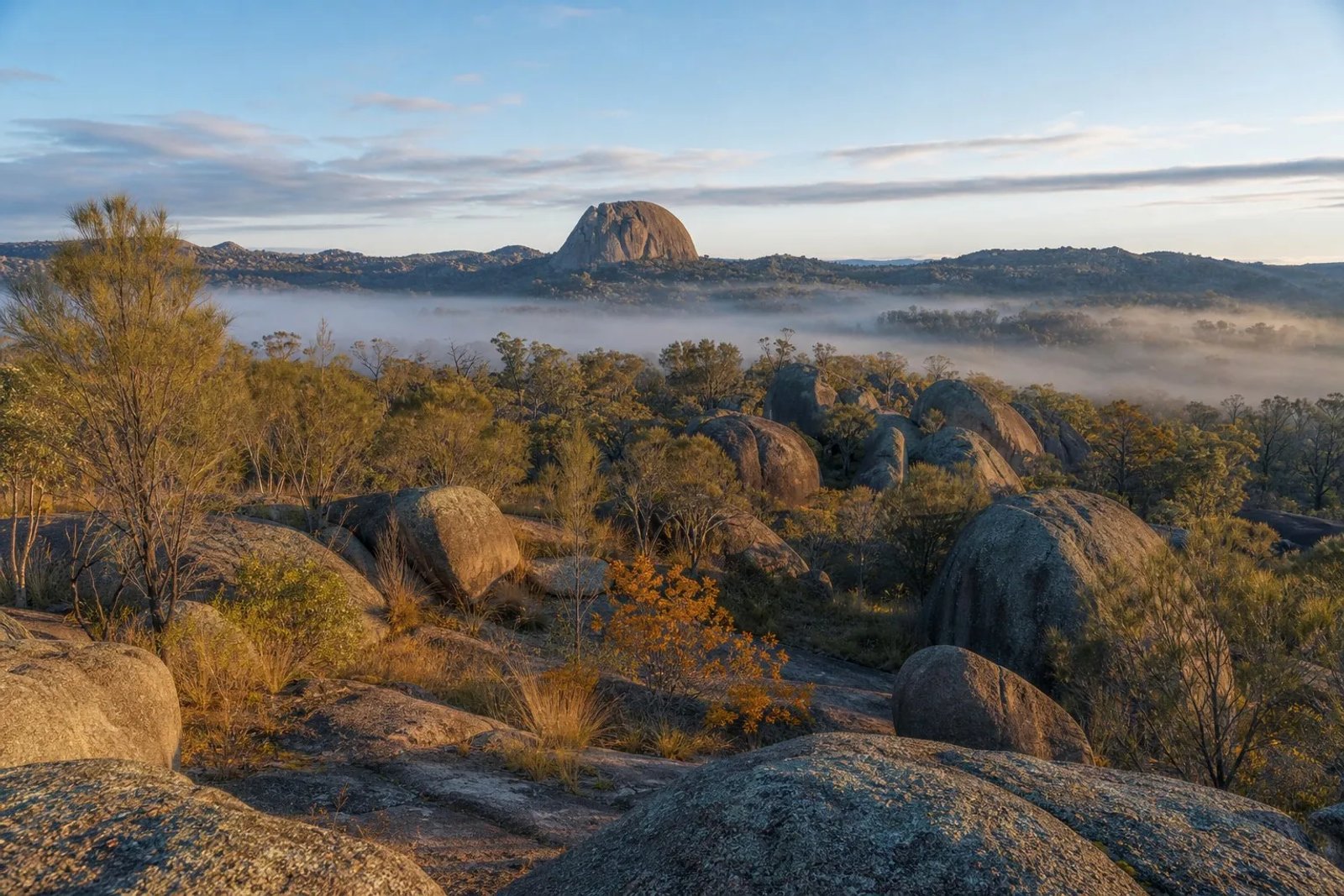 Winter landscape of Girraween National Park near Stanthorpe, Queensland, with massive rounded granite boulders, a granite dome on the skyline, golden she-oaks and thin valley mist in low afternoon light