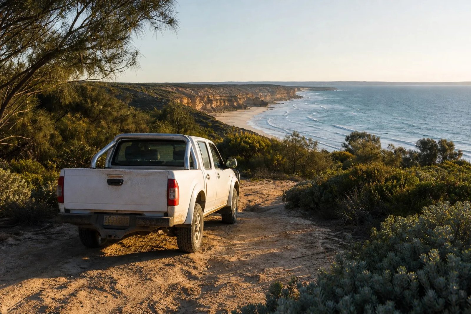 White dual-cab ute parked on a sand track overlooking the Southern Ocean coastline in Little Dip Conservation Park near Robe, South Australia, in low winter golden light