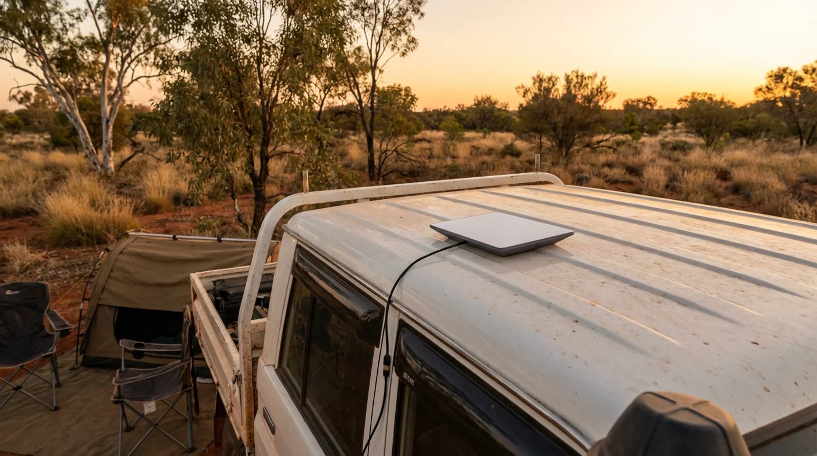 Starlink Mini magnetically mounted flat on the roof of a white LandCruiser ute at an outback Australian campsite at golden hour
