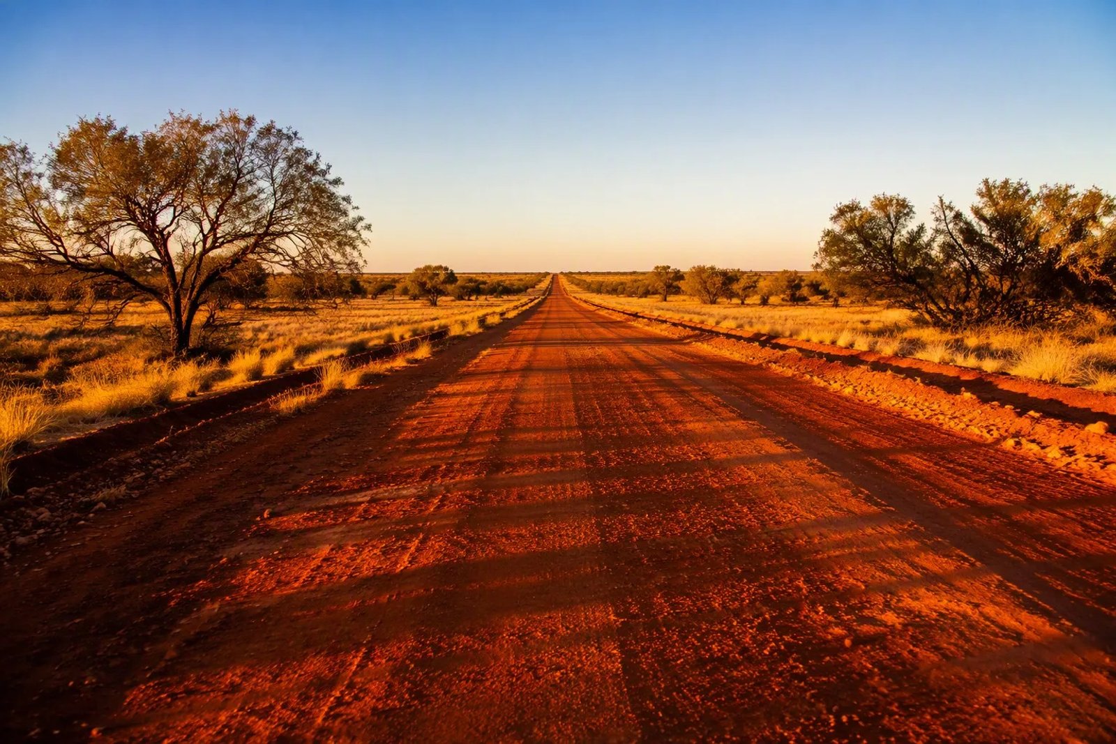 The straight ochre-red Adventure Way road stretching toward the horizon in Outback Queensland near Thargomindah at golden hour.