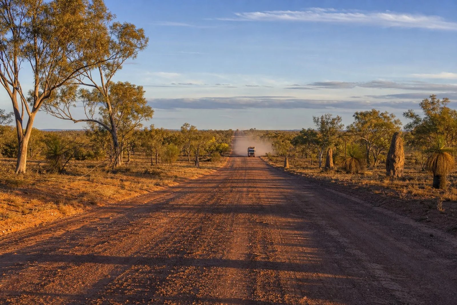 The Savannah Way red-earth road through Gulf Country, Queensland at golden hour with eucalypts, grass trees and magnetic termite mounds