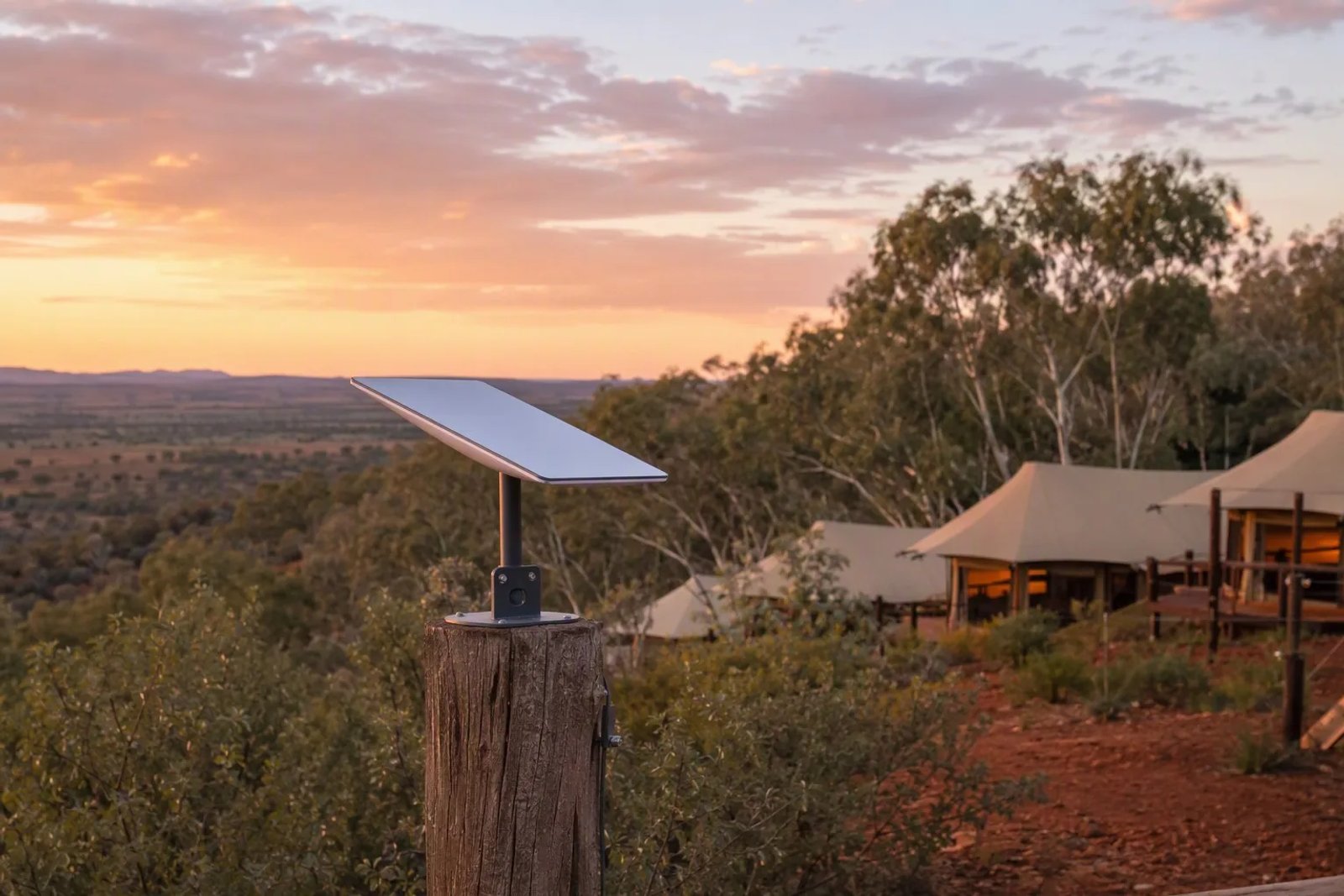A Starlink Mini dish mounted on a rustic wooden post at a luxury Australian remote glamping resort at sunset, with eco-tents in the background.
