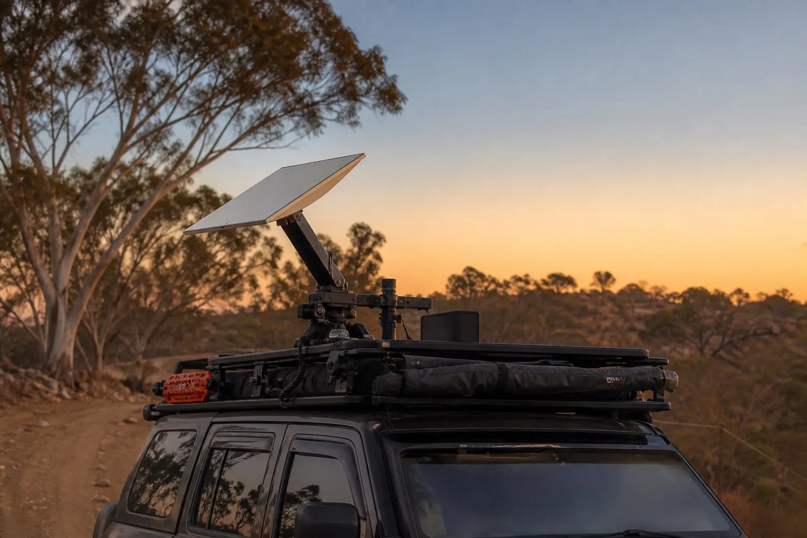 A Starlink Mini dish mounted on the roof rack of a rugged camera-tracking vehicle at a remote Australian film production location at golden hour.