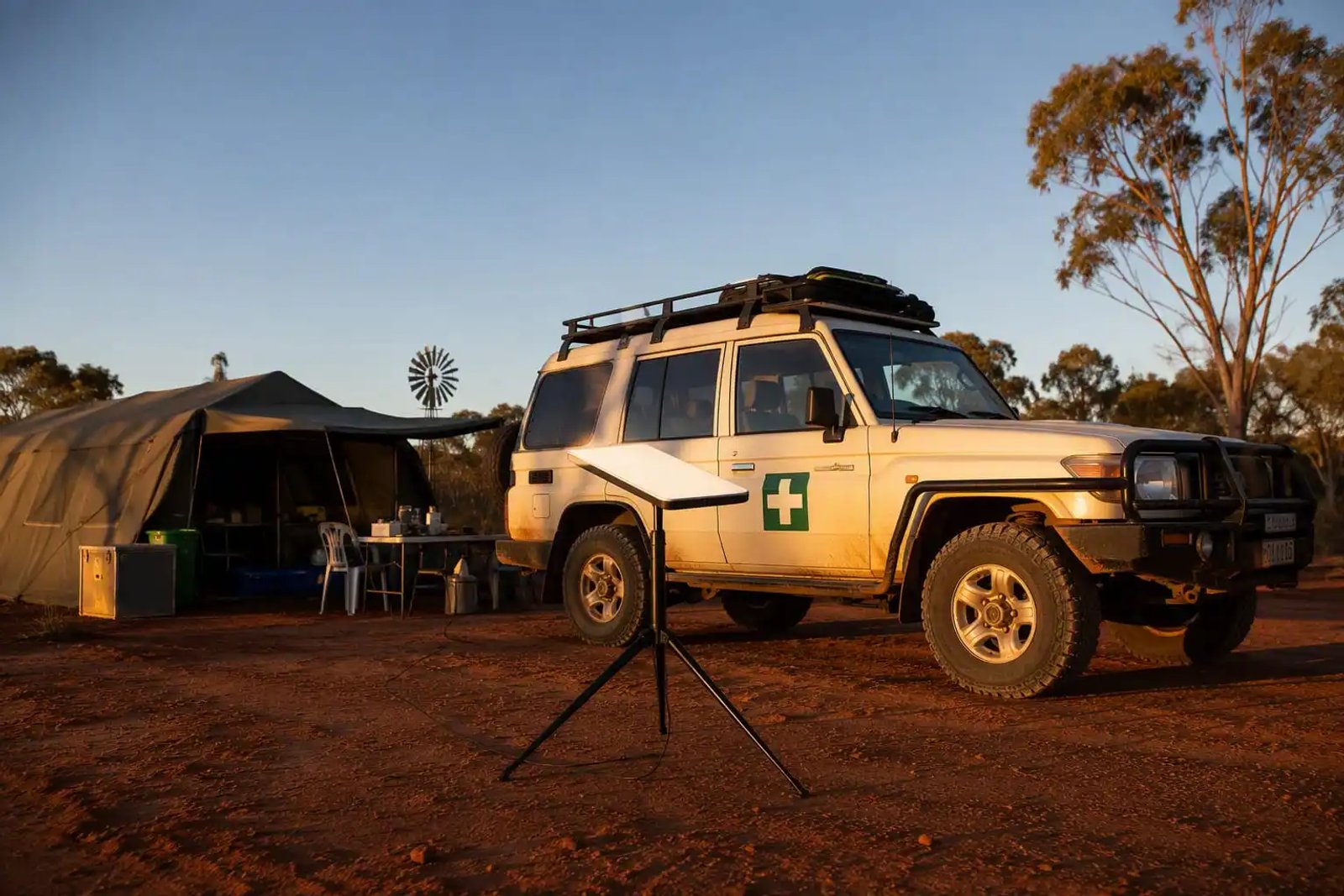 A Starlink Mini dish on a tripod beside a first aid vehicle and medical tent at a remote Australian outback worksite at golden hour.
