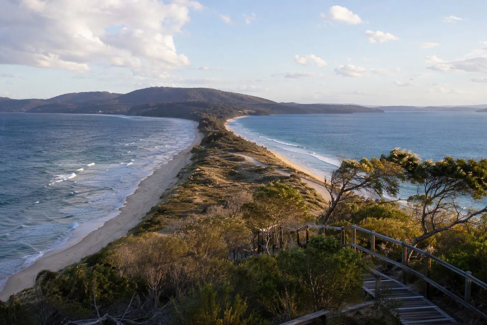 The Neck on Bruny Island: a narrow sandy isthmus with ocean on both sides, windswept coastal scrub and a wooden boardwalk, under a pale winter sky