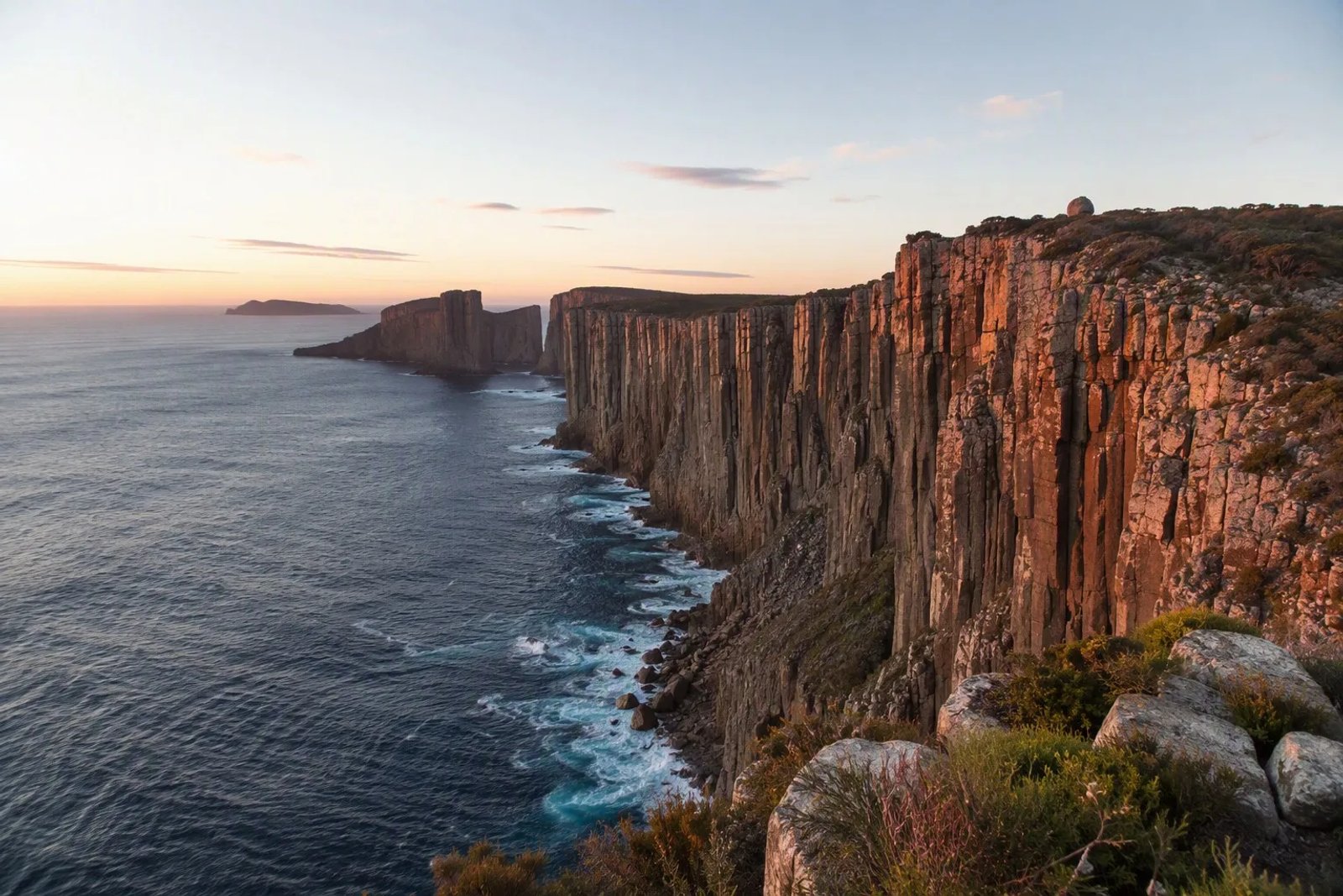 The massive dolerite sea cliffs at Cape Hauy on the Tasman Peninsula, Tasmania, glowing in the soft morning light at sunrise.