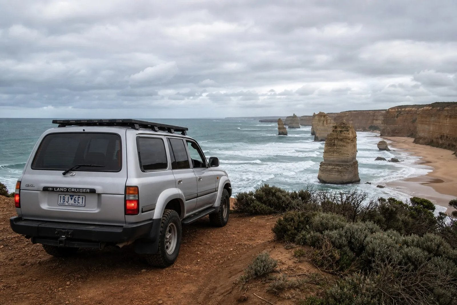 A Southern Right Whale breaching off the Shipwreck Coast near Portland, Victoria, with limestone cliffs in the background.