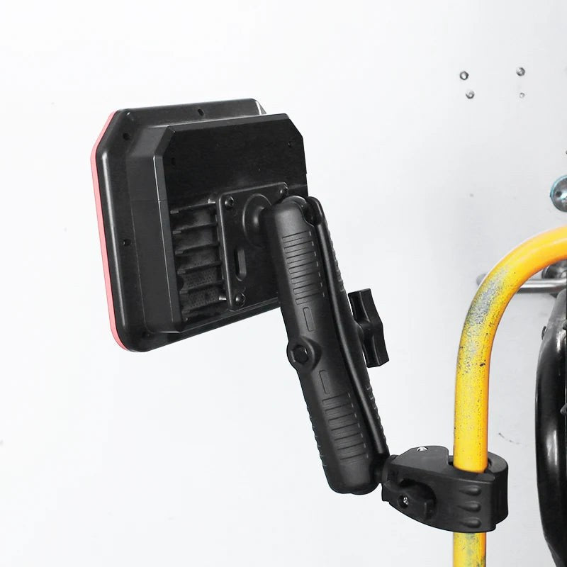 Installed example: the 230mm long arm holding a portable work light, mounted to a yellow handrail tube clamp in a workshop or service environment